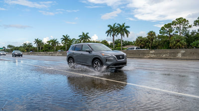 A hire car sending up a large spray of water while driving on a flooded Florida motorway