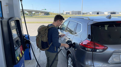 A person refueling a car rental at a gas station in Pennsylvania with signs for Philadelphia Airport visible