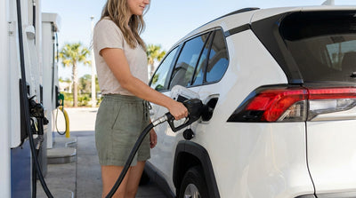 A person holds a fuel pump nozzle while refueling a modern car hire at a sunny gas station in Orlando