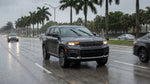 A car hire with its headlights on drives down a wet, palm-tree-lined street during a rainstorm in Miami