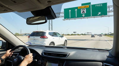 A driver's view from a car rental on a sunny Texas highway approaching a large green sign for a toll road ahead
