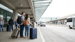 Travelers with luggage waiting at the car rental shuttle pickup zone outside San Francisco Airport Terminal 3