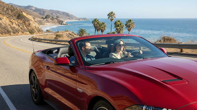 A red convertible car rental driving along the scenic coast of California on a sunny day