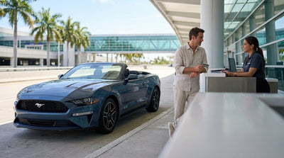 A red convertible car hire parked on a sunny street lined with palm trees in Miami