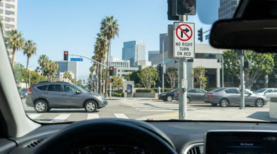 A car hire stopped at a red light on a sunny, palm-lined street in Los Angeles