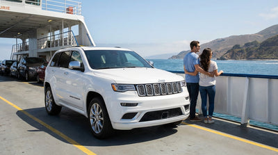 A silver car rental parked on the deck of a ferry with the sunny California coastline visible across the water