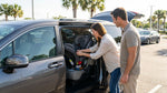 A parent installing a child seat in the back of a white SUV at a car hire lot in Orlando