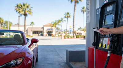 A person refuels their car hire at a sunny gas station surrounded by palm trees in California
