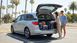 Suitcases stacked inside the open trunk of a car rental on a palm-lined street in Los Angeles