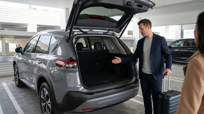A modern car hire parked with an open trunk on a hill overlooking the San Francisco skyline at sunset