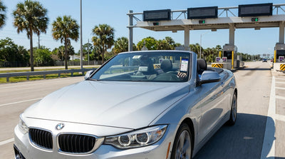 A car rental drives under an electronic toll gantry on a sunny highway lined with palm trees in Florida