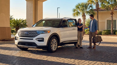 A red sedan from a car hire service drives down a long, straight road in the Texas desert at sunset
