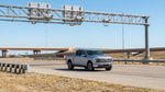 A car hire vehicle drives on a multi-lane Texas highway approaching an electronic toll gantry