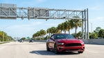 White car rental driving under an electronic toll gantry on a sunny Florida highway