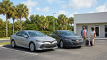 A standard sedan and a full-size car rental parked side by side under sunny Florida palm trees
