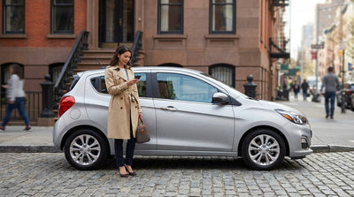 A silver car hire vehicle drives through a busy street in New York City, surrounded by iconic yellow taxis
