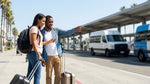 Travelers waiting for their car rental shuttle by the purple pick-up zone sign at LAX airport in Los Angeles