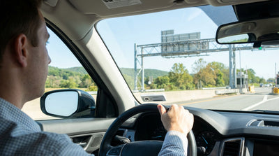 A blue car rental driving under an electronic toll gantry on a sunny highway in Pennsylvania