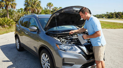 A person checks the engine oil of their Florida car hire parked on the side of a sunny road