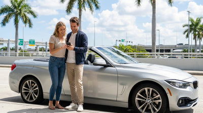A red convertible car rental driving down a palm-lined street in sunny Miami
