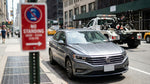 A 'No Standing' street sign on a busy New York City curb, with a car hire vehicle parked nearby