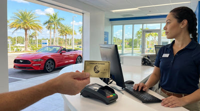 A hand holding an American Express card in front of a car hire desk at an airport in Florida