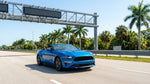 A white car rental driving under a SunPass toll gantry on a sunny multi-lane highway in Florida