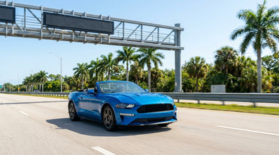 A white car rental driving under a SunPass toll gantry on a sunny multi-lane highway in Florida