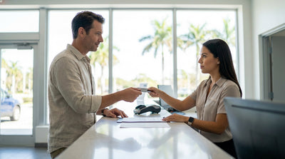A driver holds a credit card and looks at their car hire vehicle under palm trees on a sunny Florida day