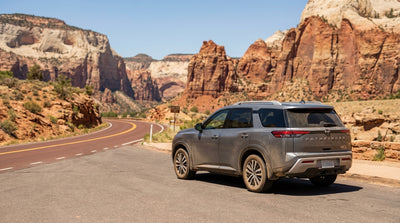 A car hire SUV drives on the scenic road leading to the Zion-Mount Carmel Tunnel entrance between red rock cliffs