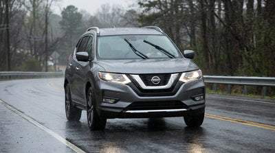 A dark-colored car rental with its headlights on, driving on a wet highway during a downpour in Pennsylvania