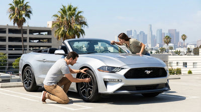A person kneels to inspect the tyre of a modern car rental on a sunny street in Los Angeles