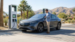 White electric car rental plugged into a public charging station on a sunny palm-lined street in California