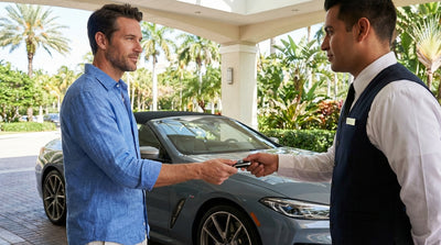A valet parks a luxury car rental in front of a sunny Miami hotel entrance with palm trees