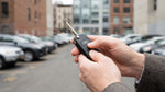 A person's hand holding and inspecting a car rental key fob on a street in New York