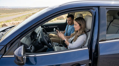 A person uses a smartphone in the driver's seat of a car rental parked on a hill overlooking the Los Angeles skyline