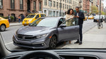 A car rental driving across the Brooklyn Bridge towards the iconic New York City skyline on a sunny day