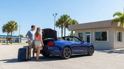 A convertible car hire drives down a scenic coastal highway in Florida, with palm trees and a bright blue sky