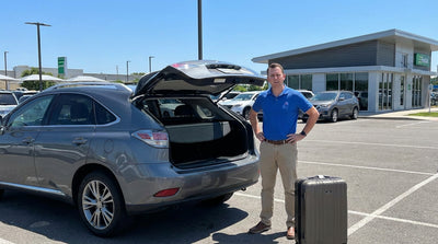 A traveler stands by their luggage, unable to open the stuck boot of their silver car rental in a sunny Orlando parking lot