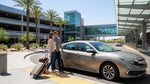 Travelers with luggage walk towards the entrance of the Las Vegas car rental center on a sunny day