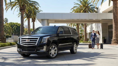 A shiny black Cadillac Escalade, a luxury car rental, parked on a street with palm trees in sunny Los Angeles