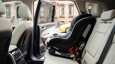 A parent installs a child car seat in the back of a car rental on a street in New York City