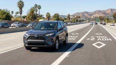 A modern car hire drives down a sunny Los Angeles freeway with traffic in the other lanes next to the HOV lane