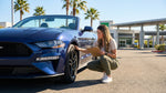 A person inspects a shiny blue sedan for their car hire at a sunny parking lot in Las Vegas