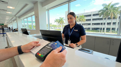 A convertible car hire drives down a sunny, palm-lined street with colorful Art Deco buildings in Miami