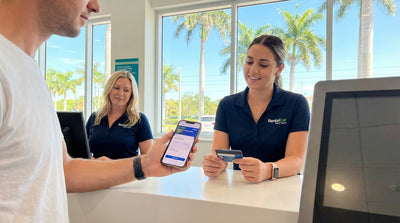 A person holds a smartphone next to their convertible car hire on a sunny, palm-lined road in Florida