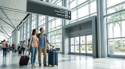 Travelers with luggage wait by the curb for a car rental shuttle bus at LAX in Los Angeles