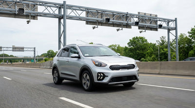 A car rental drives on a highway in New York, approaching an electronic E-ZPass toll gantry under a sunny sky