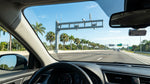 A white car rental driving under a SunPass electronic toll gantry on a sunny Florida highway