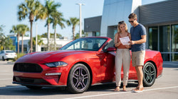 Two people in the front seats of a car rental driving along a sunny palm-lined road in Florida